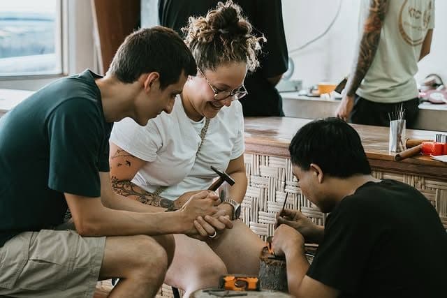 Friends laughing while shaping silver at the workbench